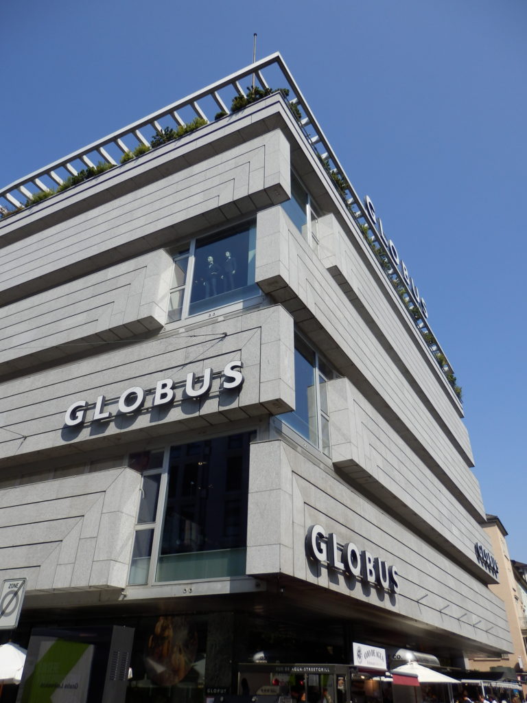 Gebäude Kaufhaus Globus in Rohbeton. Verschachtelte, horizontale Fassadenteile in asymetrischer Ecklösung im Wechsel mit Fensteröffnungen