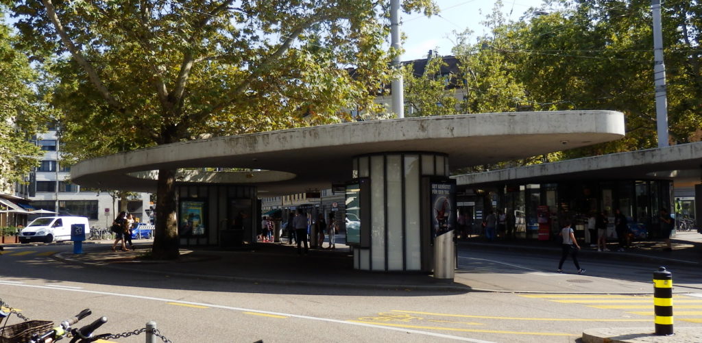 Tram-Pavillon mit runden Kiosken und amorpher Deckenplatte (Beton) und ausgespartem Bereich durch dem ein Baum wächst.